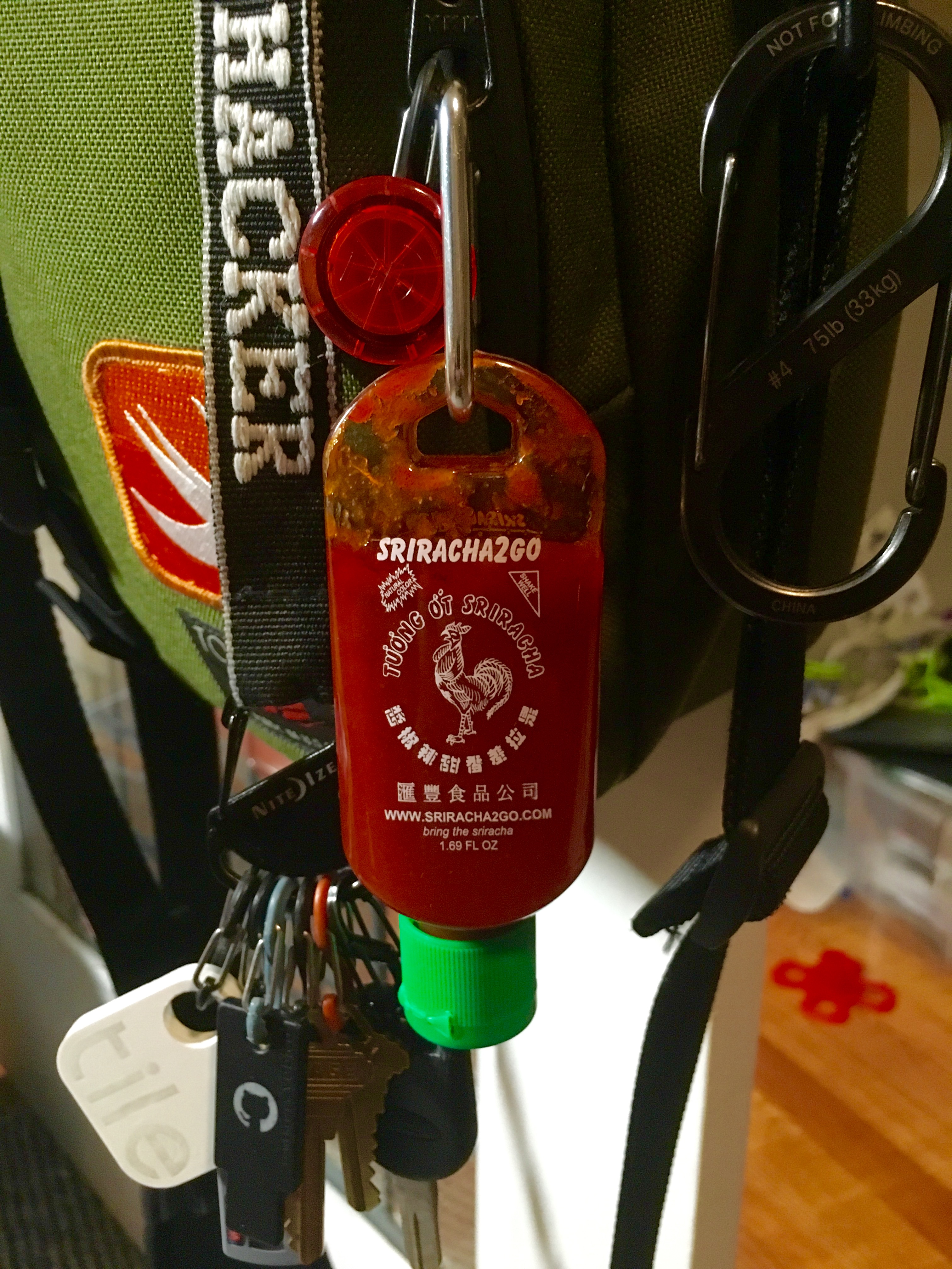 'Small Sriracha bottle attached to messenger bag'
